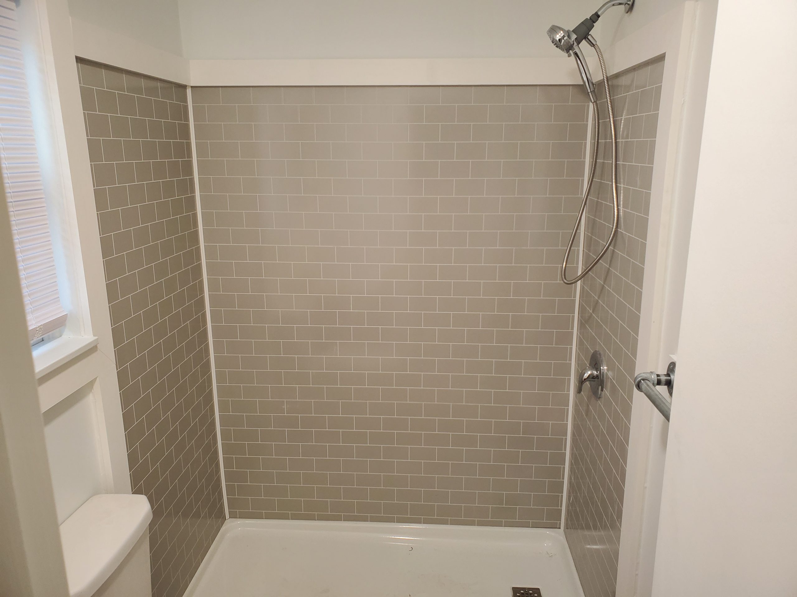Tiled shower surround with a linear tile pattern and handheld shower fixture