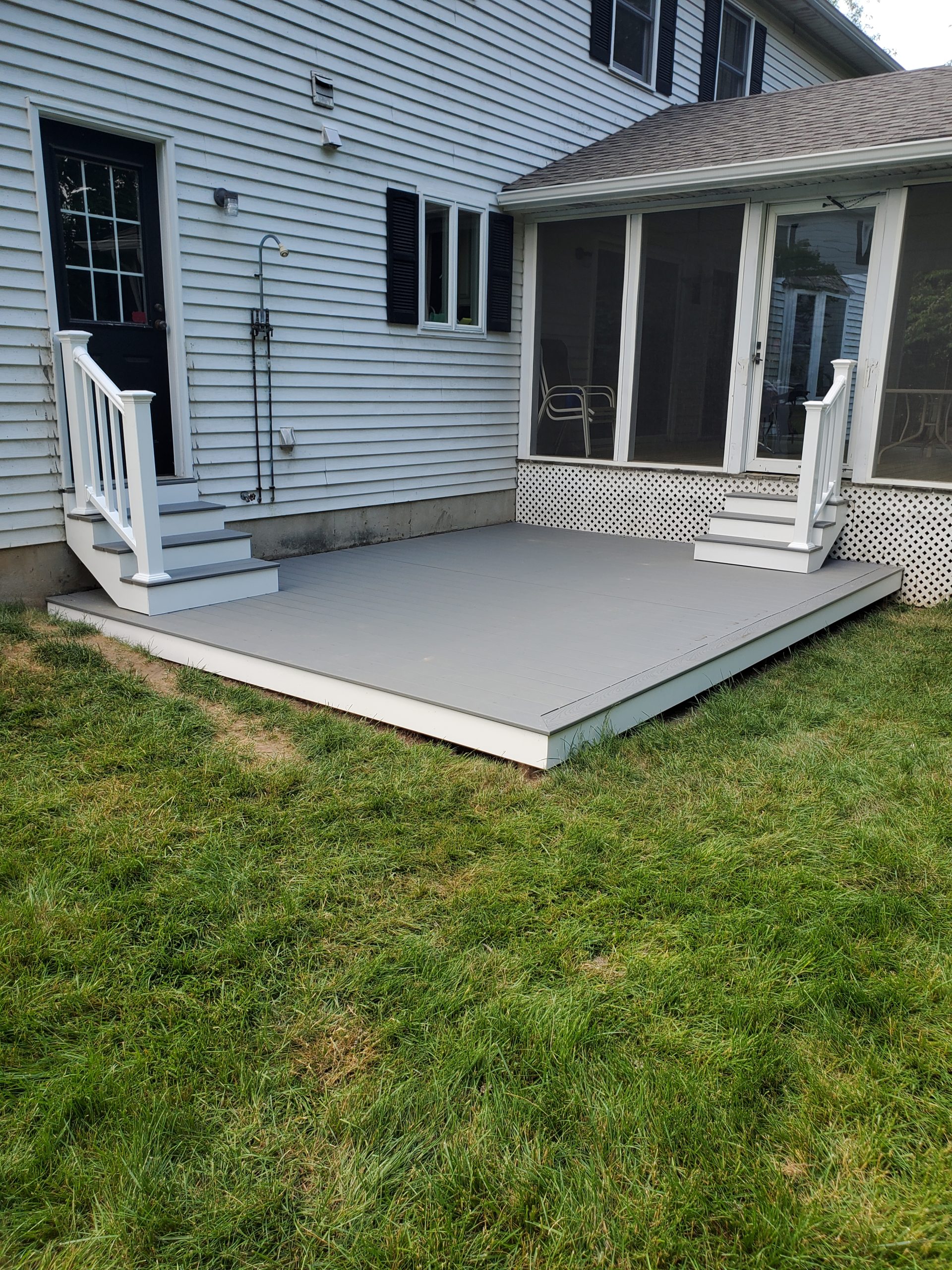 New gray composite deck platform with white railings and steps at the rear of a home