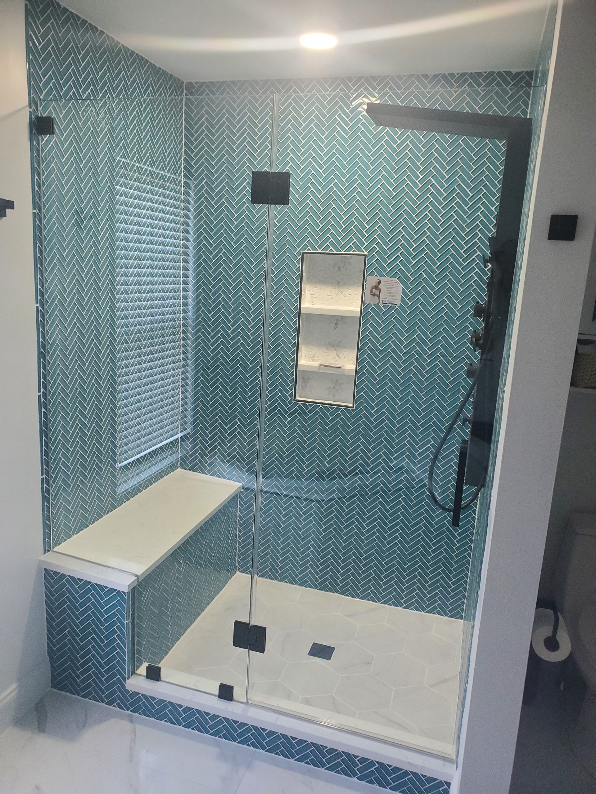 Teal herringbone tiled shower with a built-in bench and black fixtures