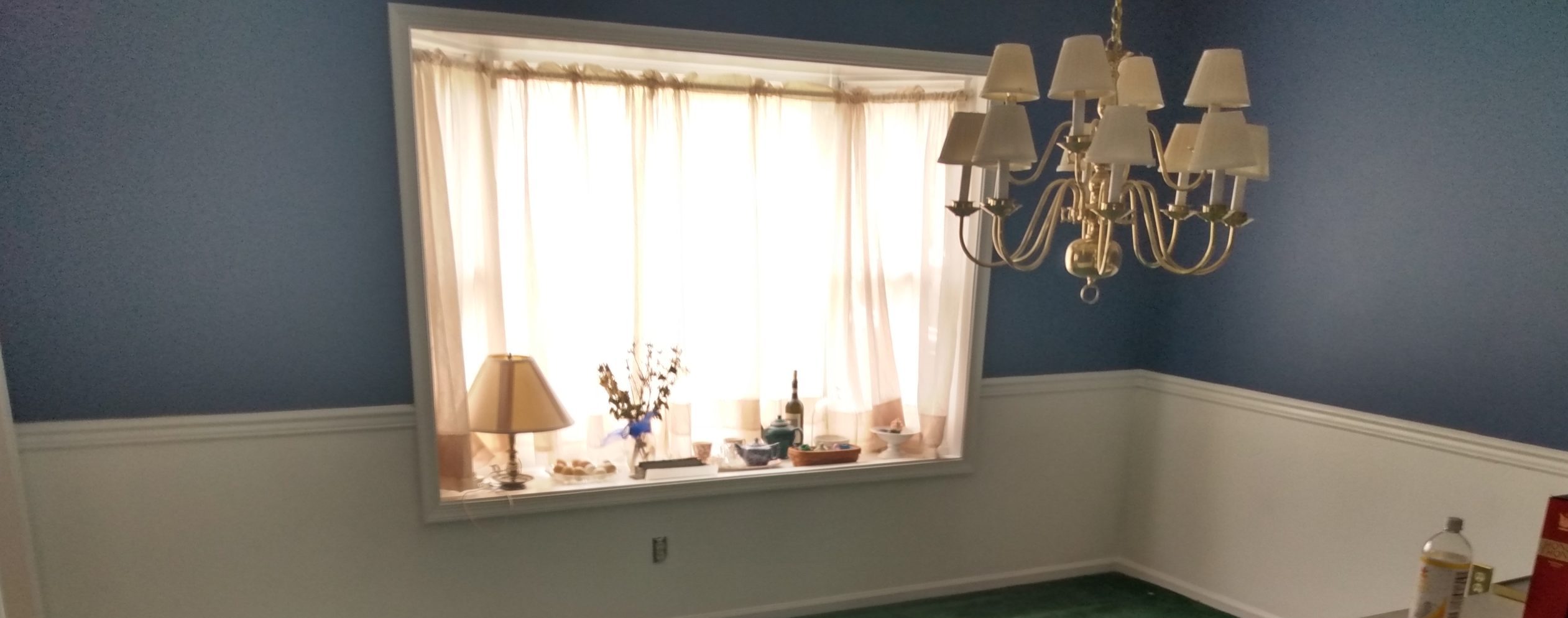 Bay window with sheer curtains and wainscoting in a blue-painted room