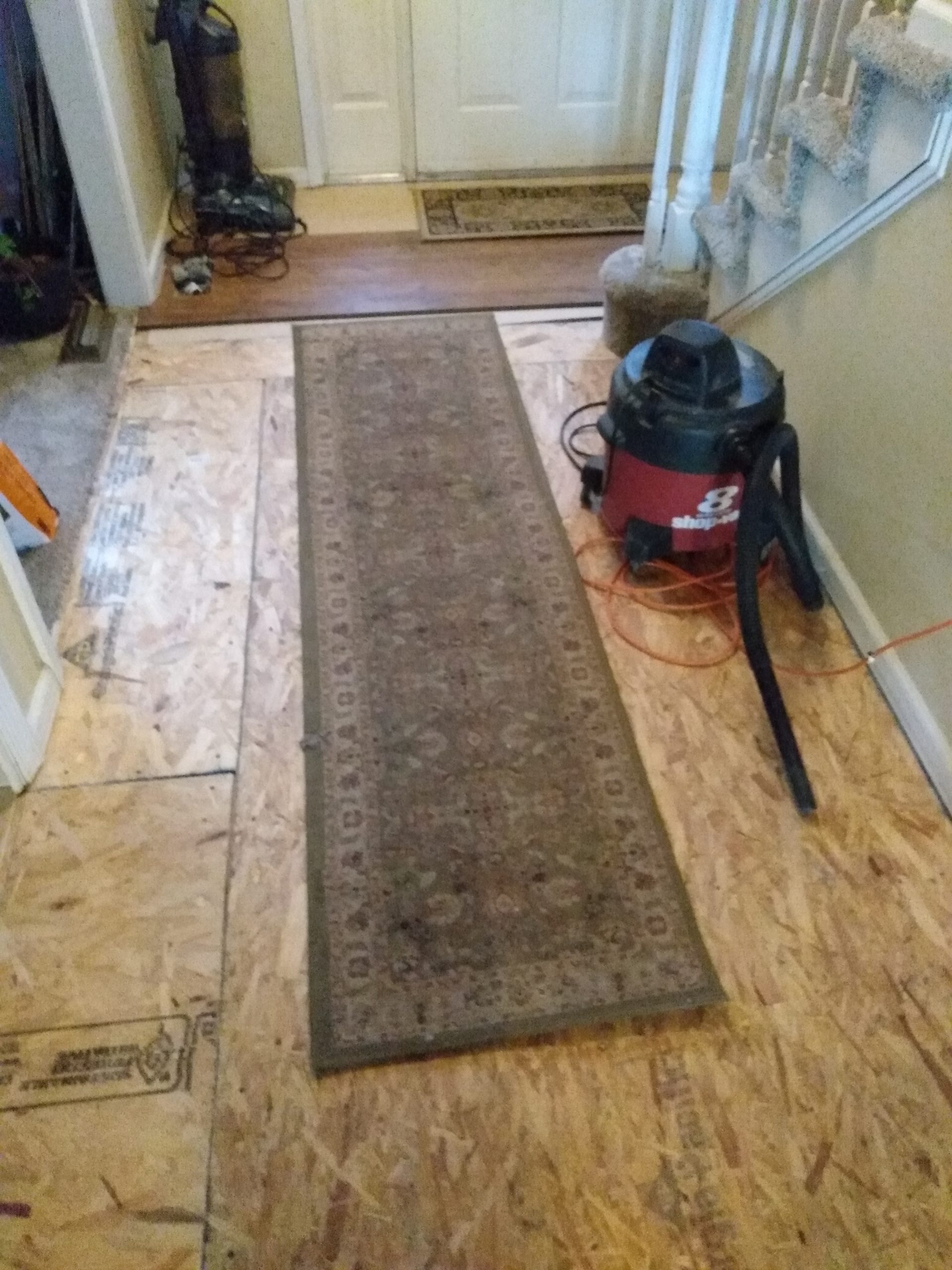 Hallway floor replacement in progress with subfloor exposed and shop vacuum
