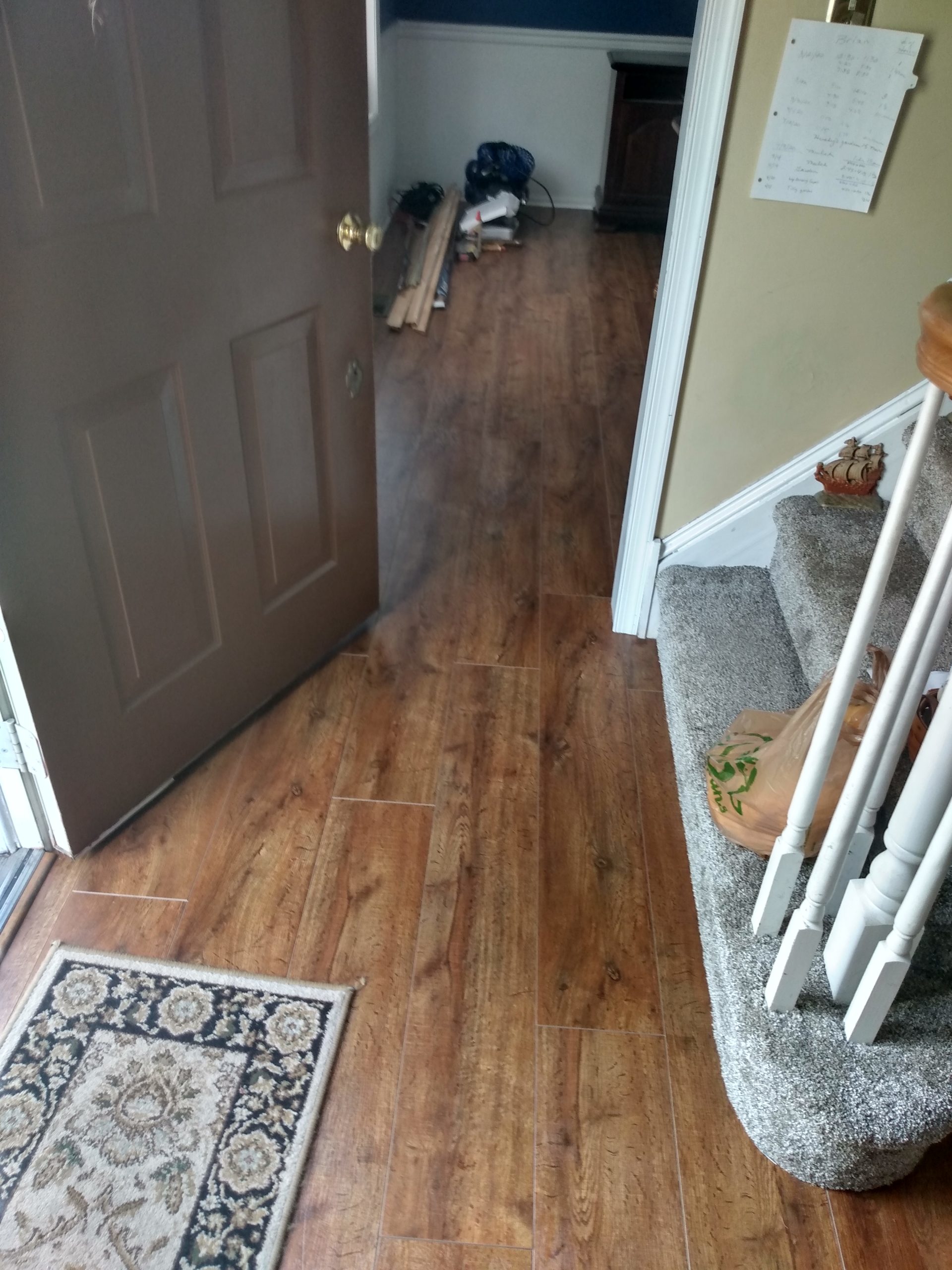 Wood-look plank flooring installed in an entryway beside a carpeted staircase