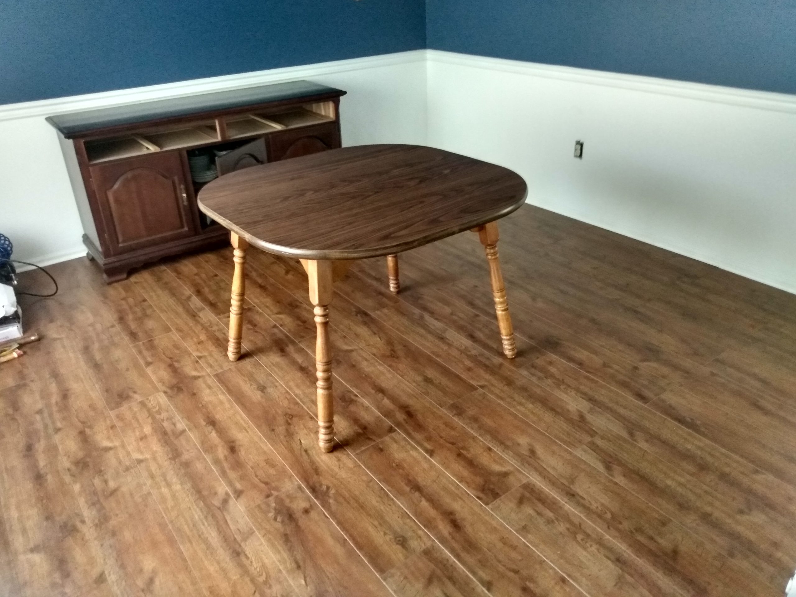 Wide-plank wood flooring in a dining area with an oval table and wood hutch