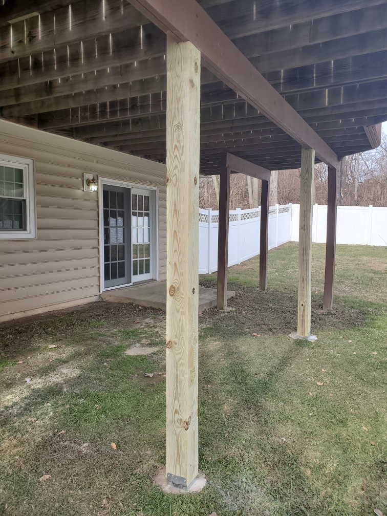Underside of a raised deck with new support posts, viewed from the yard