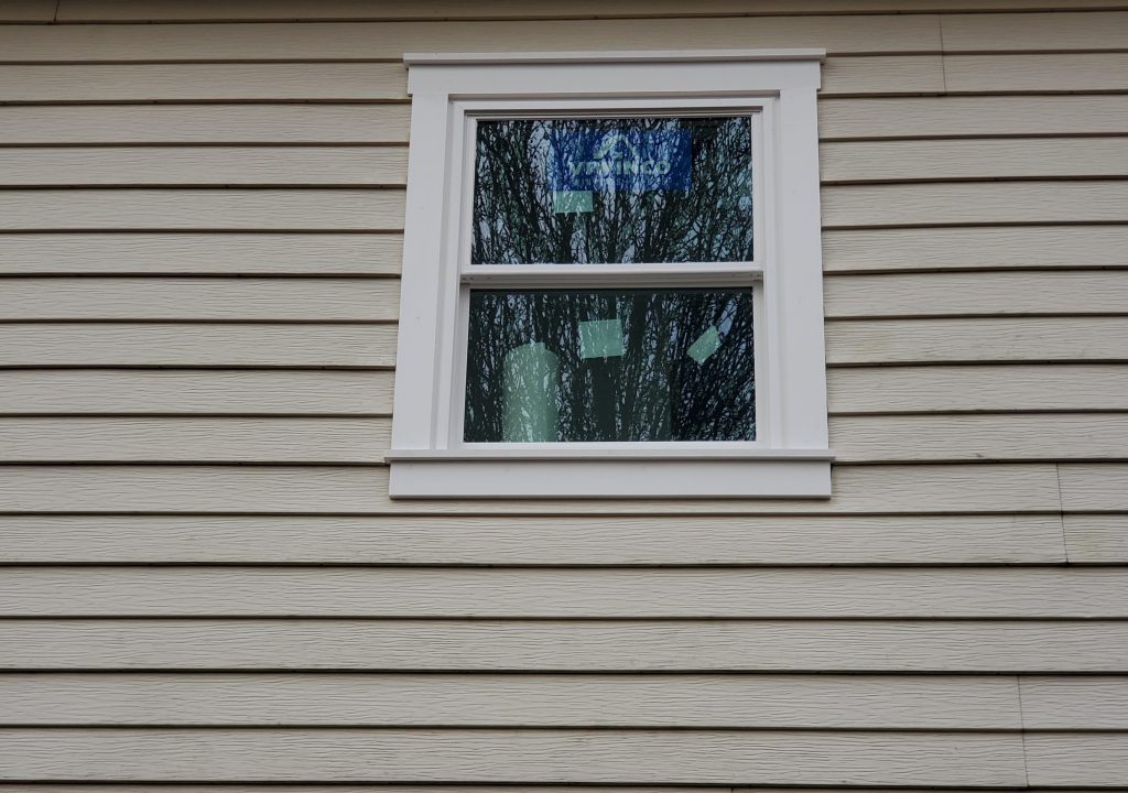 New white vinyl replacement window installed in gray clapboard siding