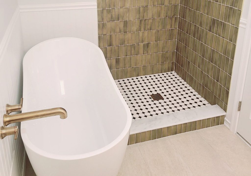 Renovated bathroom with a freestanding soaking tub, green tiled walk-in shower and brass fixtures