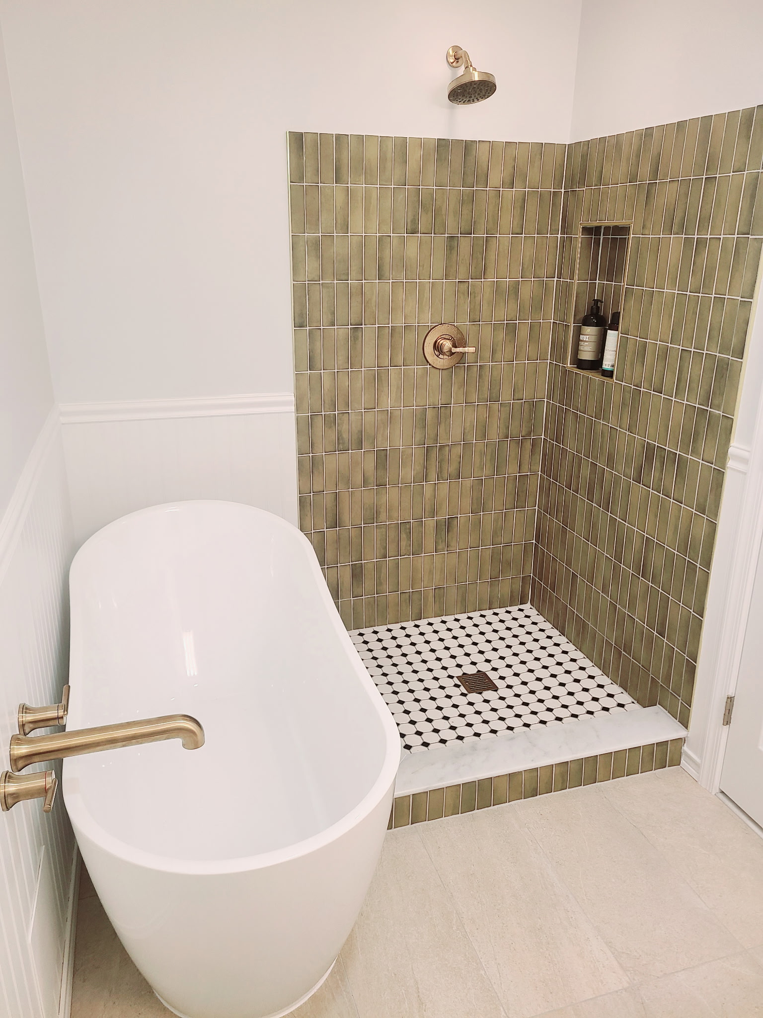 Freestanding soaking tub beside a green tiled walk-in shower with brass fixtures