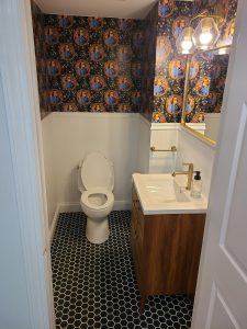 Powder room with patterned wallpaper, beadboard wainscoting, and black hex tile floor