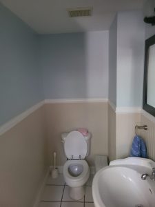 Small powder room before renovation with pale blue walls, beige wainscoting and a pedestal sink