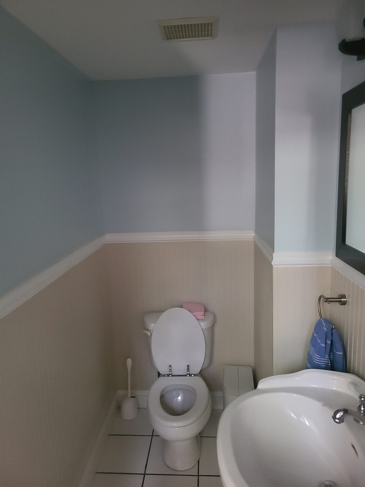 Small powder room before renovation with pale blue walls, beige wainscoting and a pedestal sink