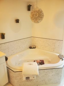 Corner jetted tub after remodel with white marble hexagon mosaic tile surround and a capiz shell pendant light