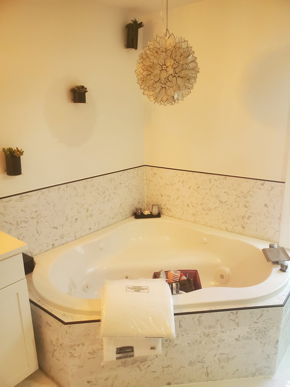 Corner jetted tub after remodel with white marble hexagon mosaic tile surround and a capiz shell pendant light