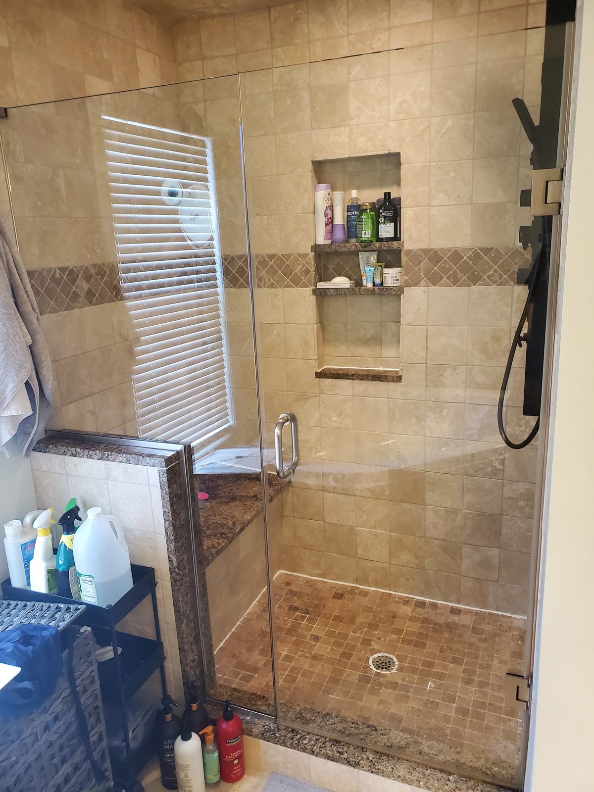 Walk-in shower before remodel with travertine tile, granite bench and framed glass door