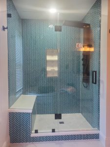 Rebuilt walk-in shower with teal herringbone glass tile, marble bench and niche, and a frameless glass door