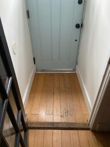 Entry vestibule before renovation with worn hardwood flooring inside the front door