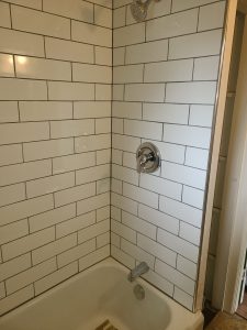 Bathtub surround tiled in white subway tile with gray grout and chrome shower fixtures