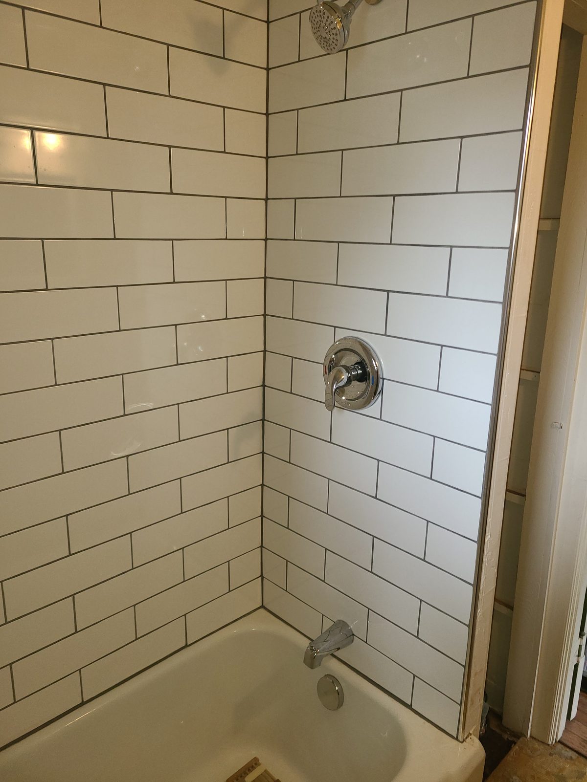 Bathtub surround tiled in white subway tile with gray grout and chrome shower fixtures