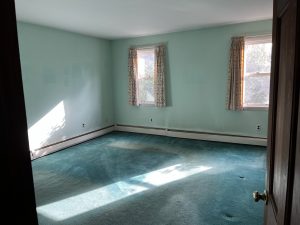Bedroom before renovation with mint green walls and worn teal wall to wall carpet