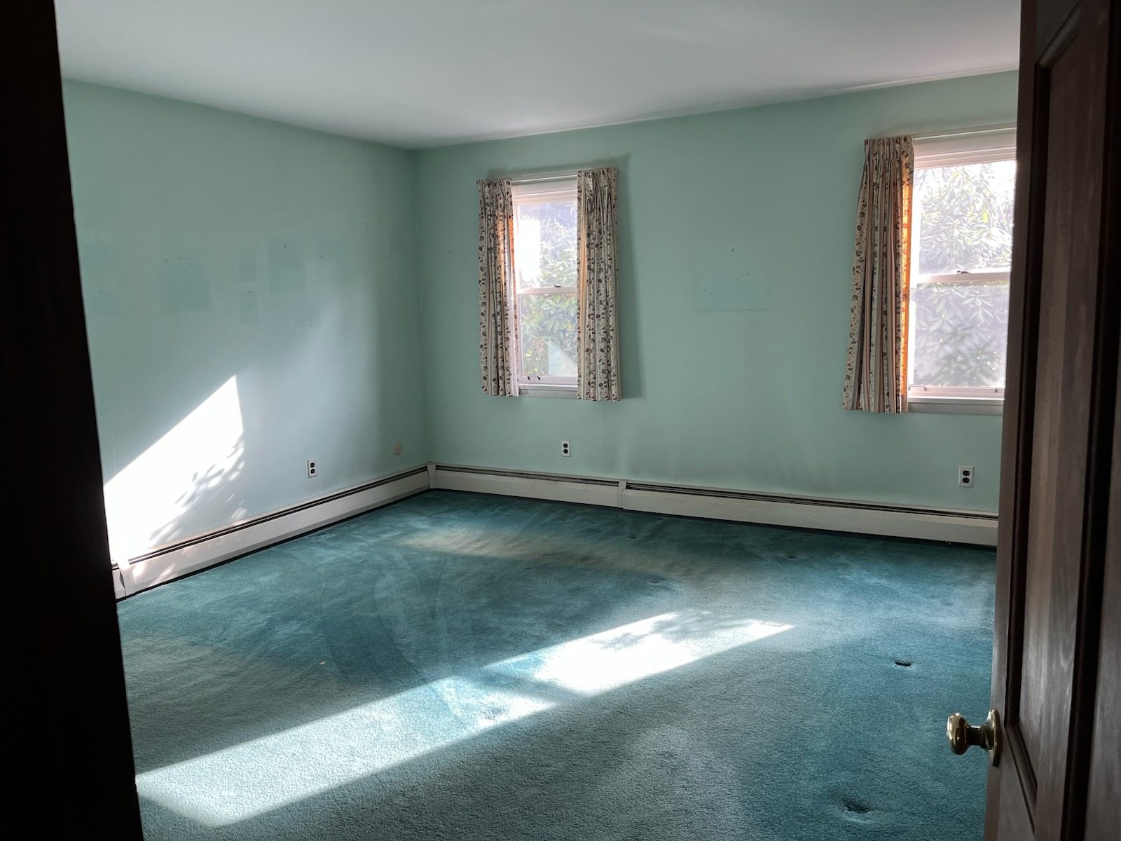 Bedroom before renovation with mint green walls and worn teal wall to wall carpet