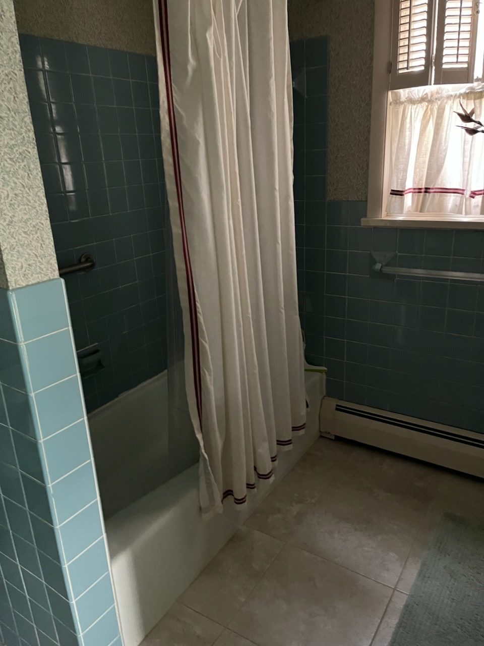 Bathroom before remodel with teal wall tile, an alcove tub and a shower curtain
