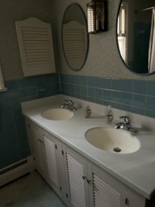 Original double vanity with louvered cabinet doors and teal wall tile before the remodel