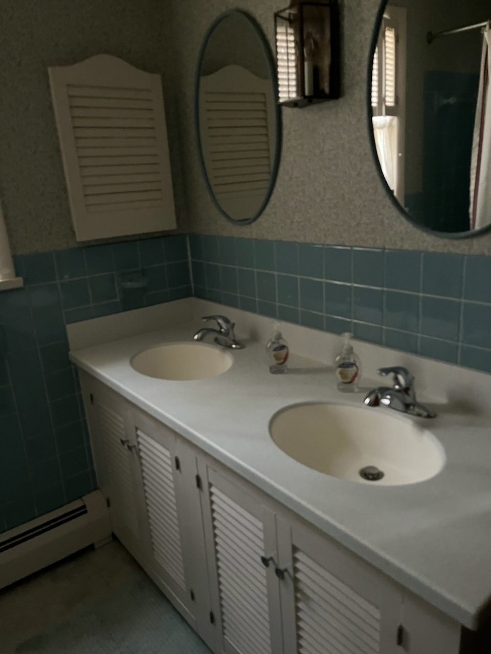 Original double vanity with louvered cabinet doors and teal wall tile before the remodel
