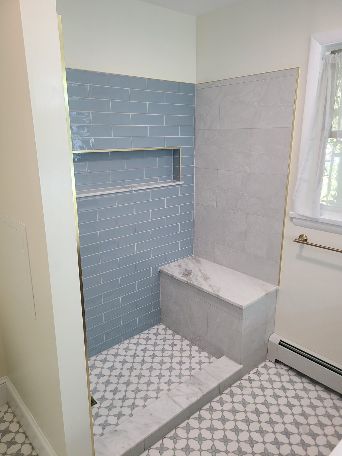 Walk-in shower with light blue subway tile, a marble bench and brass edge trim