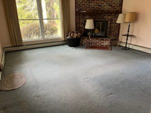 Living room before renovation with worn wall to wall carpet and a brick fireplace