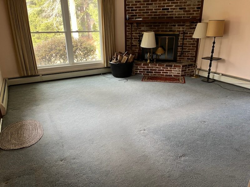 Living room before renovation with worn wall to wall carpet and a brick fireplace