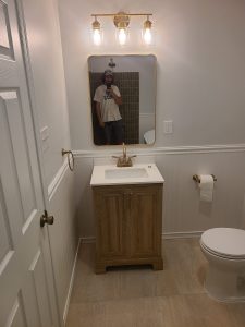 Bathroom vanity with a brushed gold three light fixture and a gold framed mirror