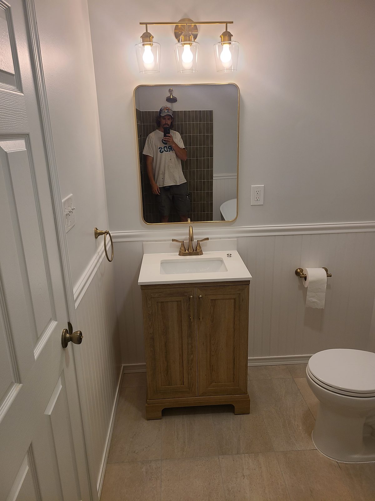 Bathroom vanity with a brushed gold three light fixture and a gold framed mirror