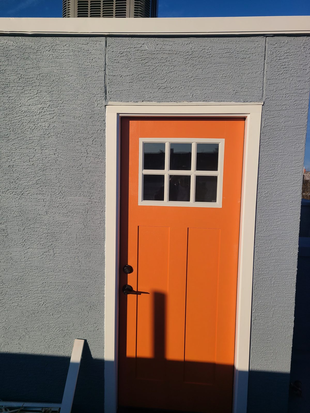 New craftsman style exterior door painted orange with white trim in a stucco wall