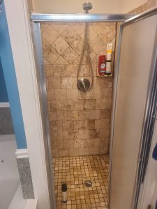 Original stand-up shower with travertine tile walls and floor and a framed glass door