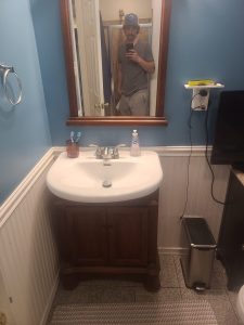 Bathroom vanity with a wood cabinet, beadboard wainscoting and blue walls before the remodel