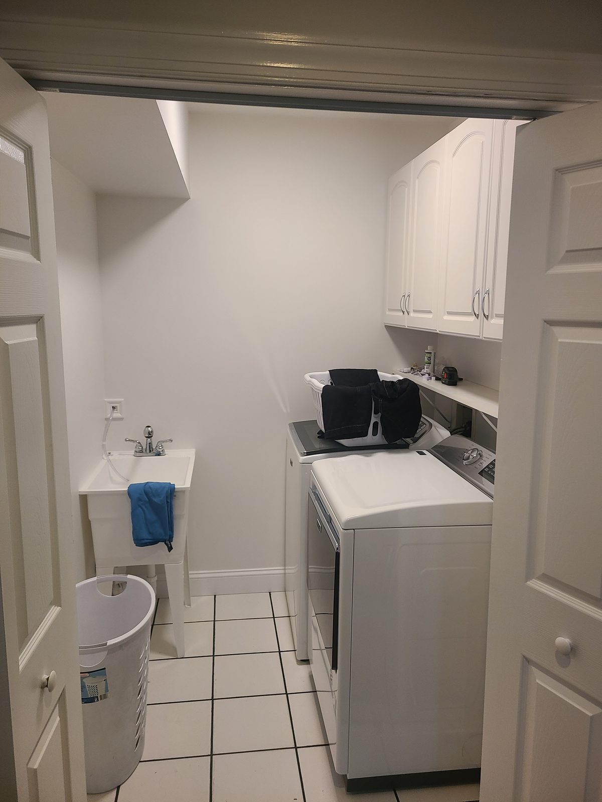 Laundry room with a utility sink, white wall cabinets and white tile flooring