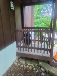 Small covered entry landing with an aging brown wood railing before the rebuild