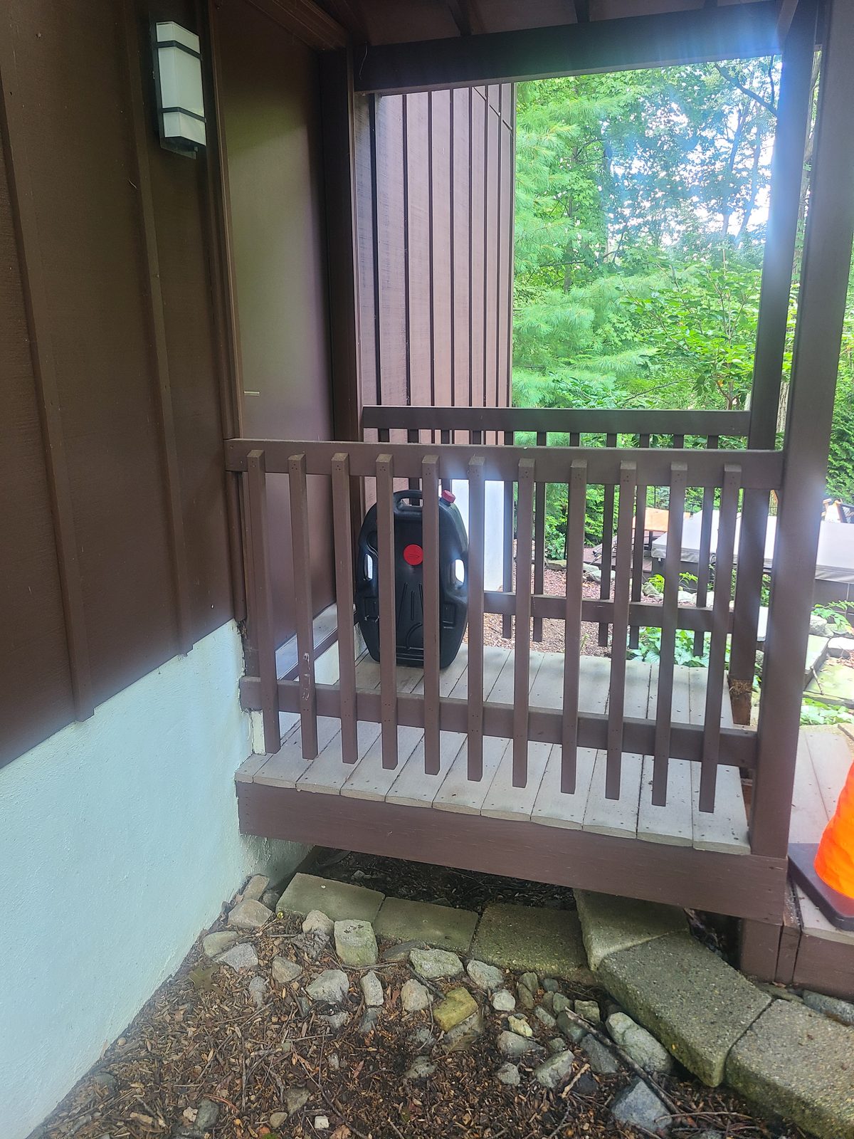 Small covered entry landing with an aging brown wood railing before the rebuild