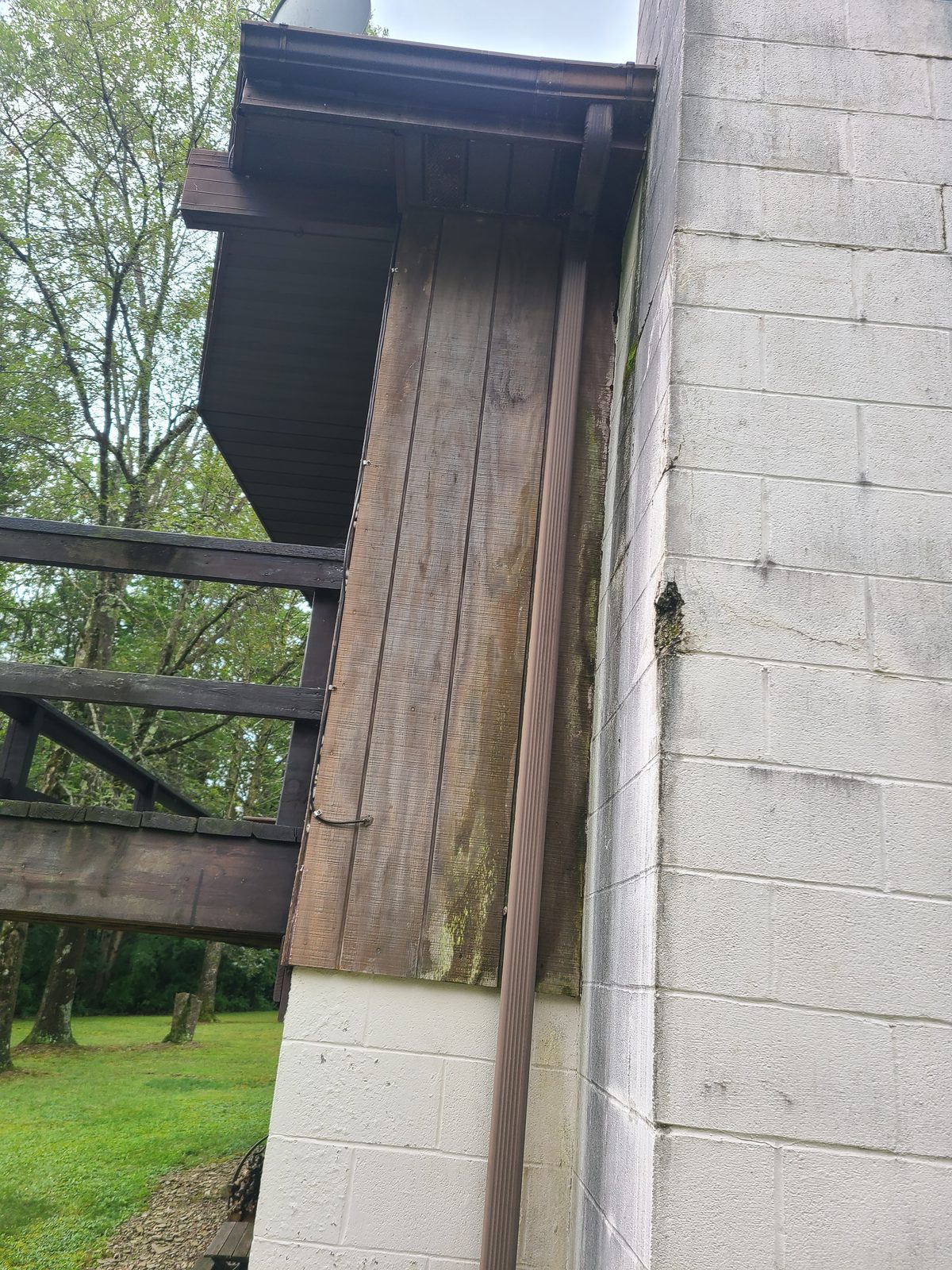 Weathered wood siding and old gutter at the chimney wall before replacement