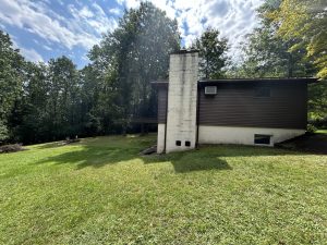 Rear exterior of the house with its original dark siding and block chimney