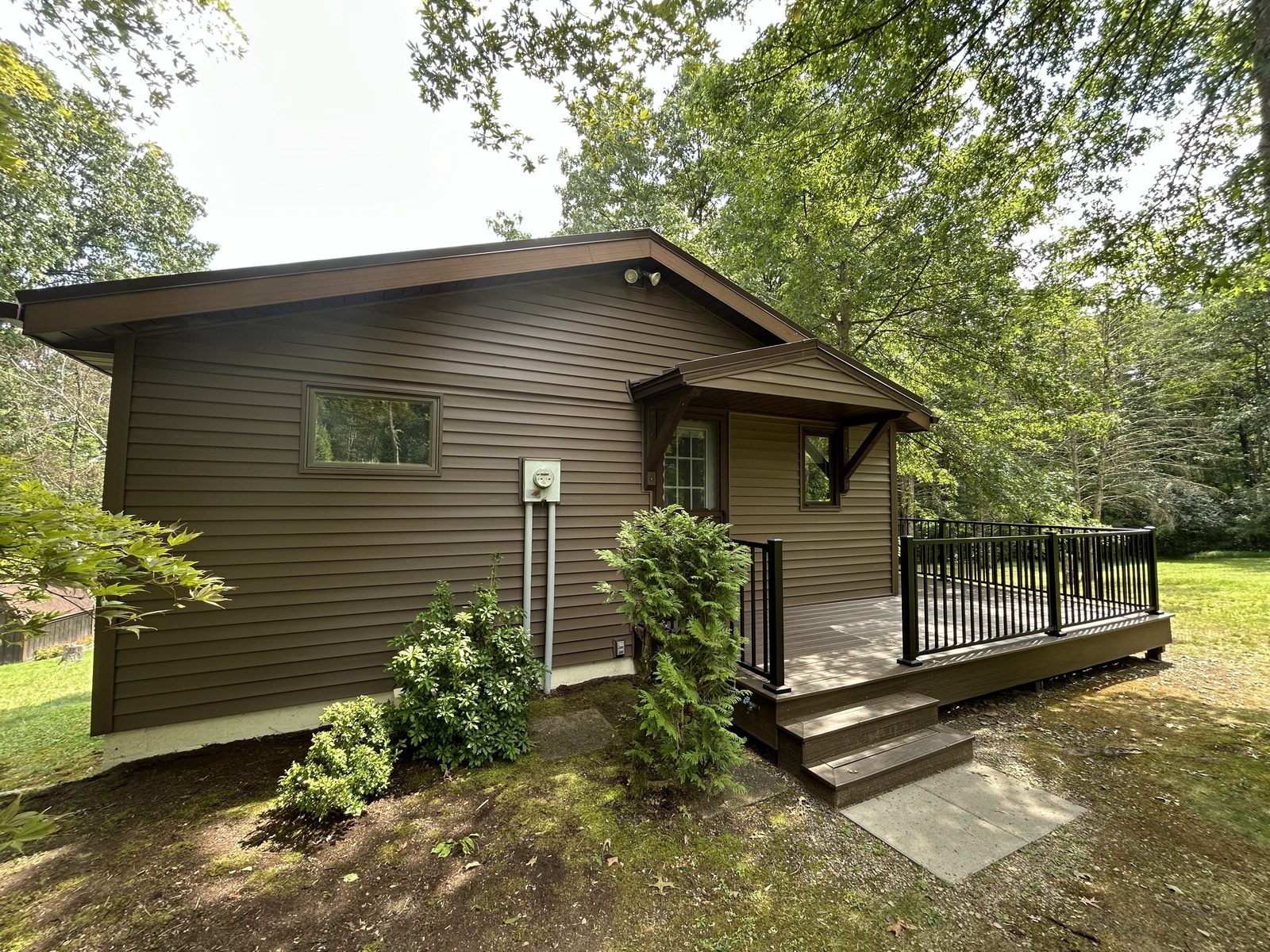 Finished exterior with new siding, a covered entry and a new deck with black railing