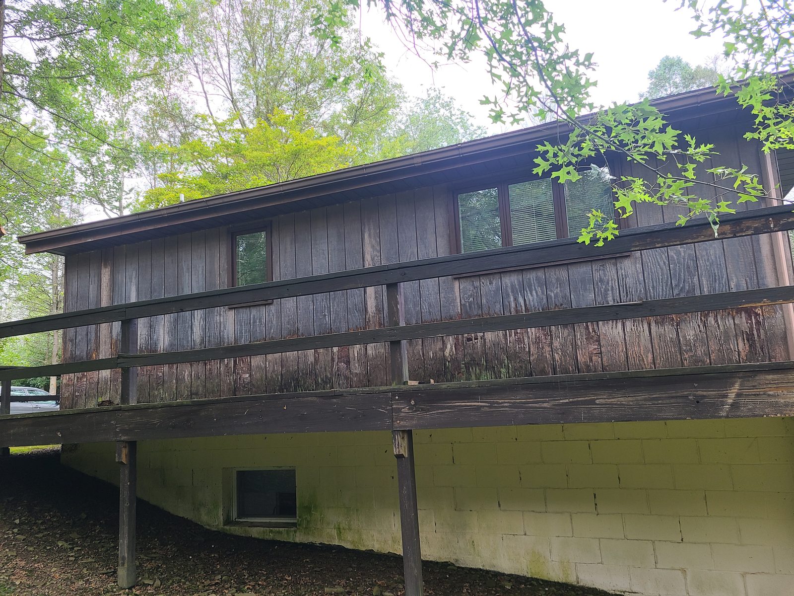 Deck side of the house before residing, showing badly weathered siding boards above the deck