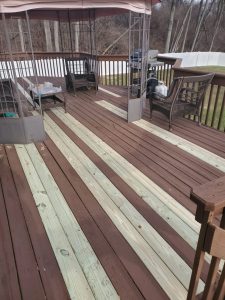 New pressure treated deck boards woven in among existing stained boards during a deck rebuild
